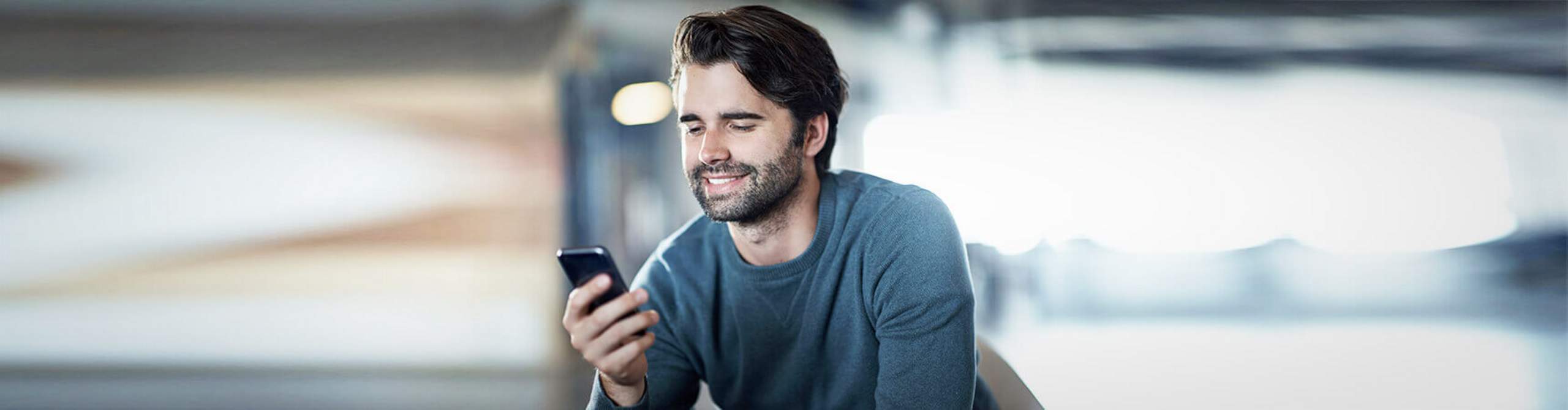 Ein Mann schaut lächelnd auf sein Smartphone.