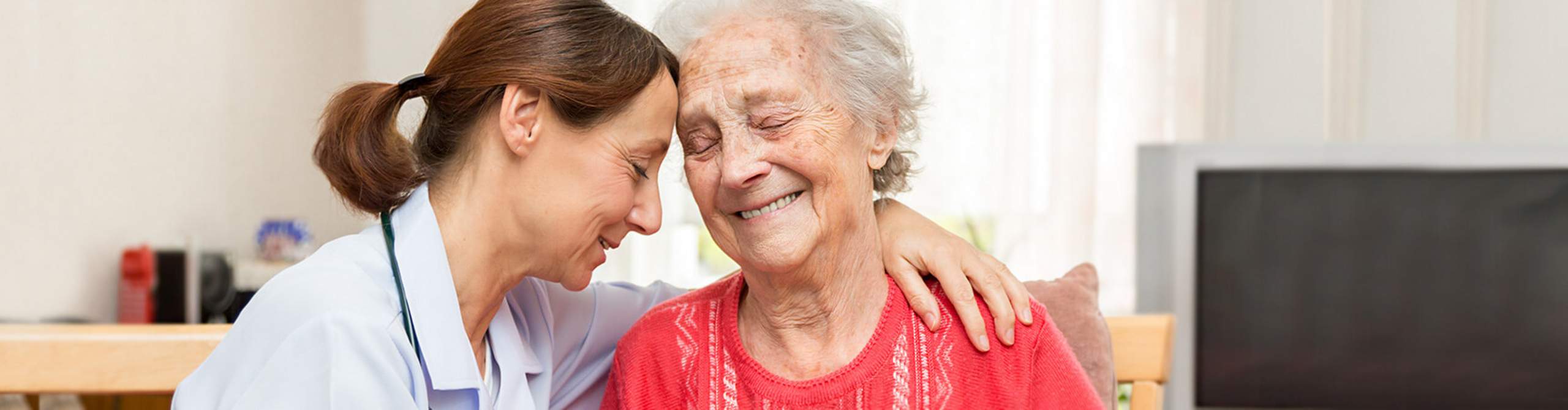 Pflegerin umarmt ältere Frau.