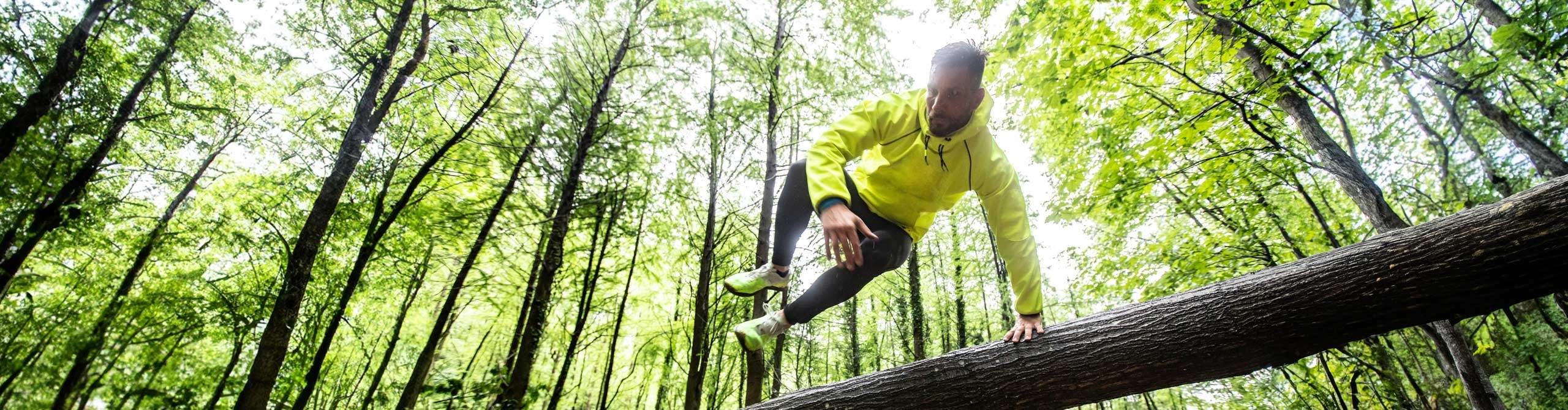 Sportler springt auf einem Waldweg über einen Baum