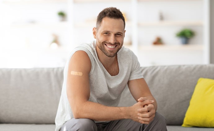 Mann sitzt mit einem Pflaster nach einer Impfung am Arm auf einem Sofa