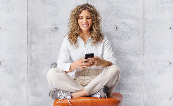 Eine Frau im Schneidersitz schaut lächelnd auf ihr Smartphone
